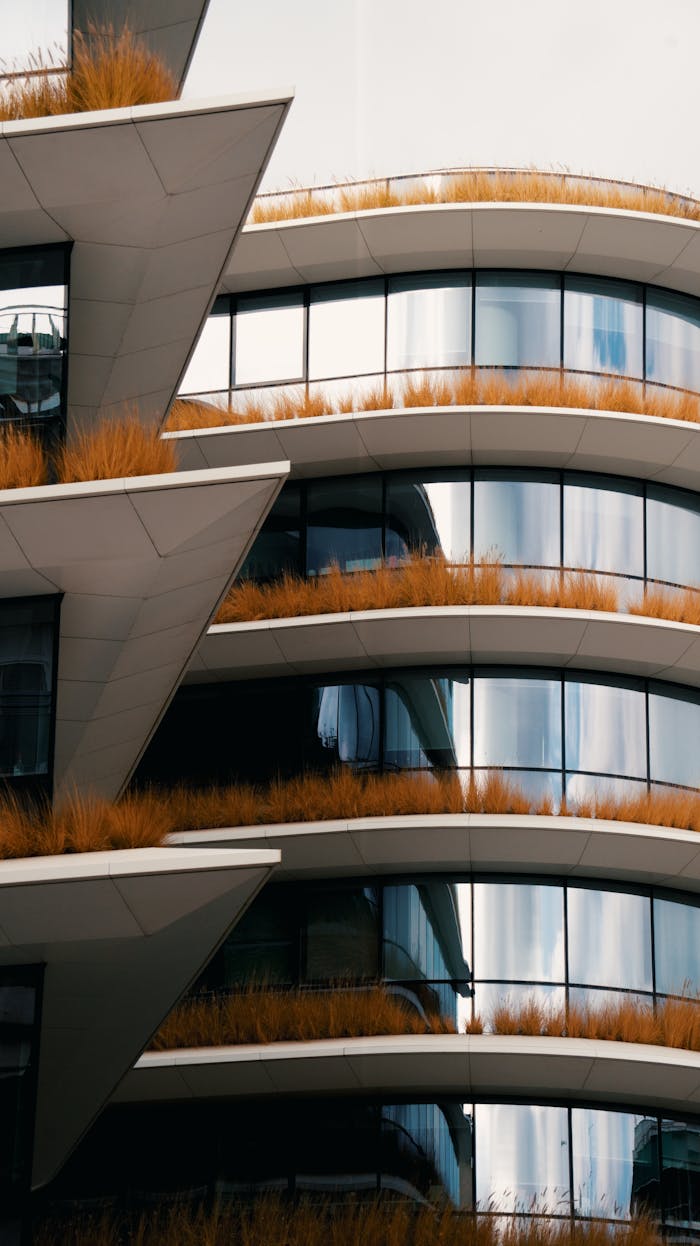 Curved modern building facade with vegetation on ledges, showcasing urban green architecture.