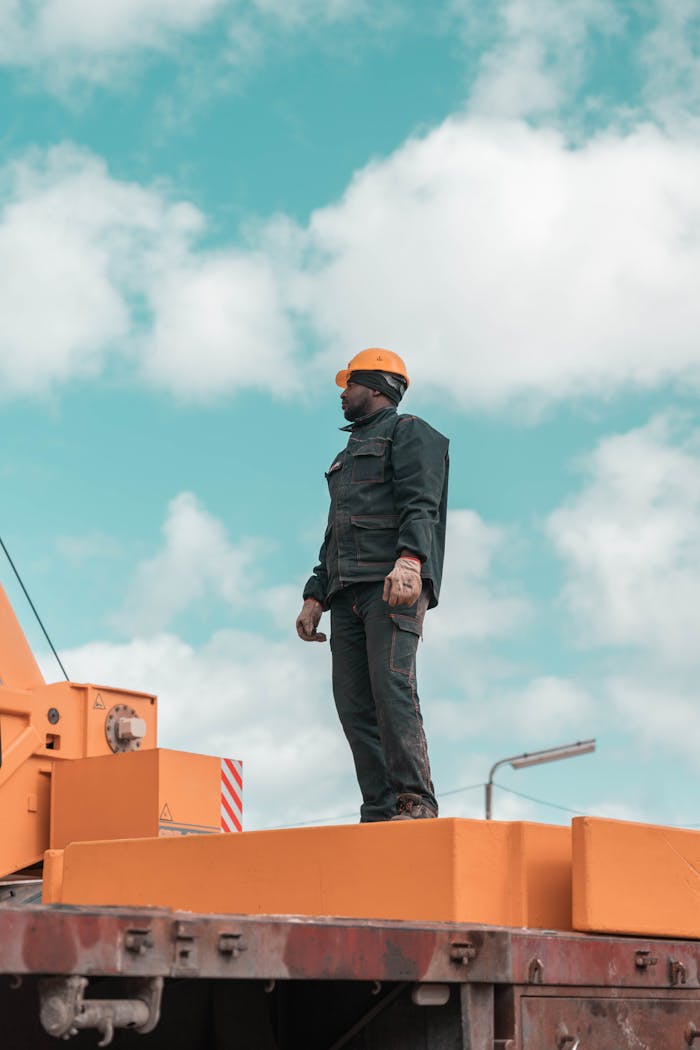 A construction worker stands on a crane against a blue sky, symbolizing strength and industry.