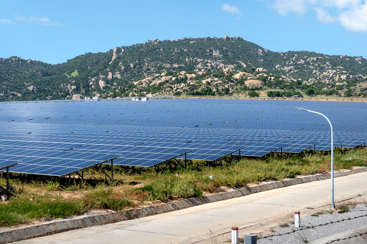 A vast solar farm set against a mountainous landscape under a blue sky.