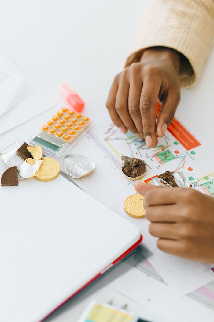 Hands arranging chocolate coins and documents, symbolizing finance and strategy.